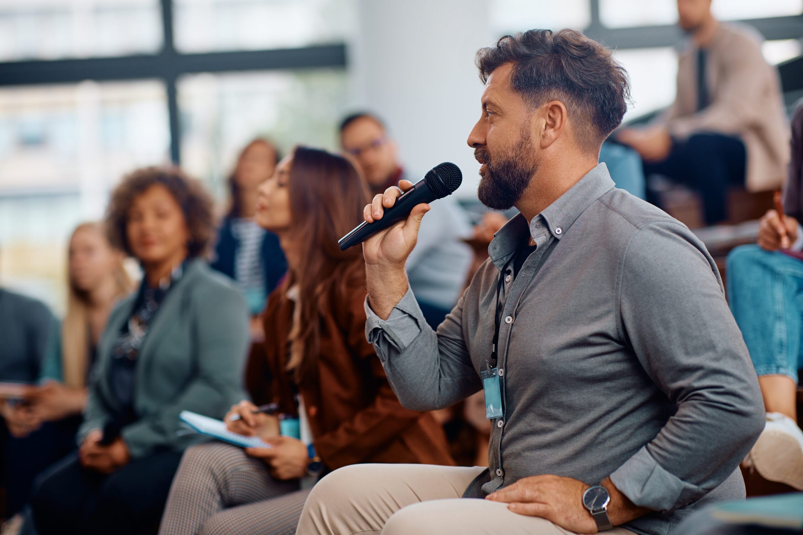 Business seminar attendee talking on microphone while sitting in the audience at convention center. Business seminar attendee talking on microphone while sitting in the audience at convention center.