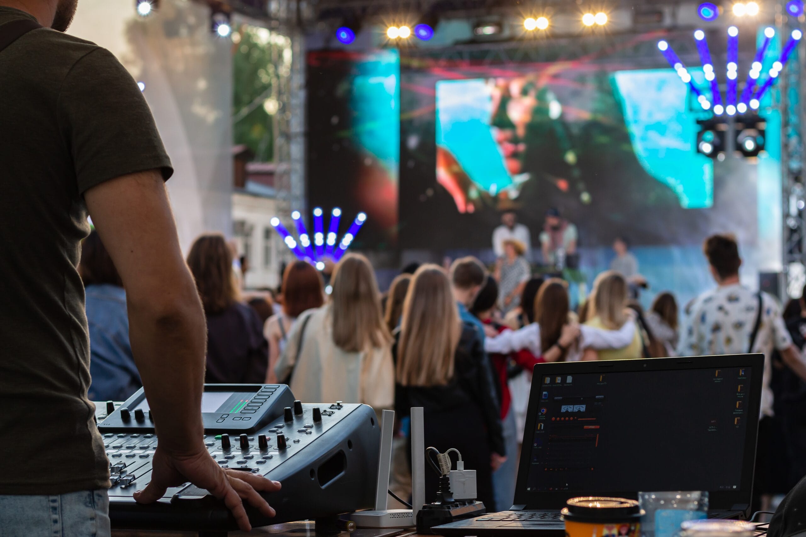 low light, professional DJ music mixer, laptop at party festival with crowd of people in background low light, professional DJ music mixer, laptop at party festival with crowd of people in background